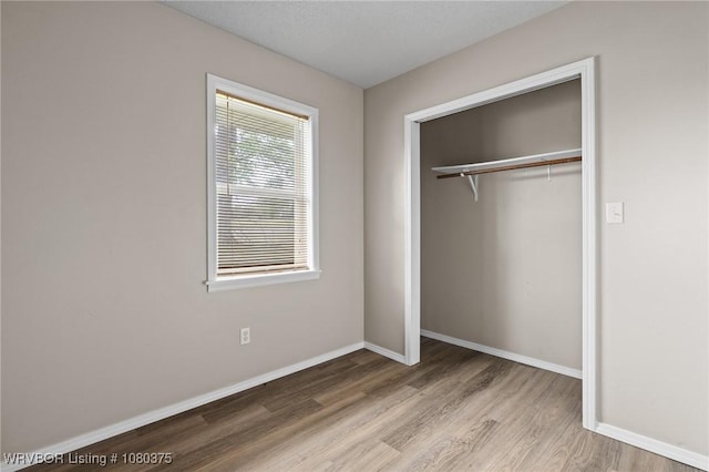 unfurnished bedroom featuring wood finished floors, a closet, and baseboards