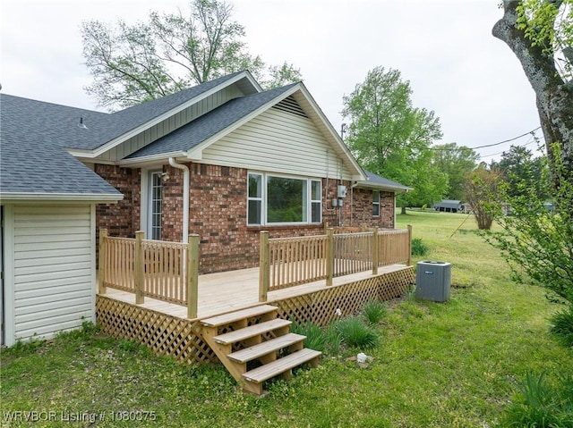 back of house with brick siding, a yard, roof with shingles, and a wooden deck