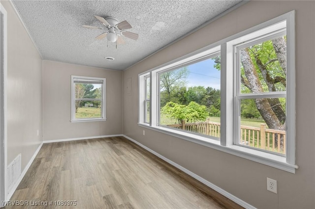 empty room featuring visible vents, wood finished floors, a textured ceiling, and plenty of natural light