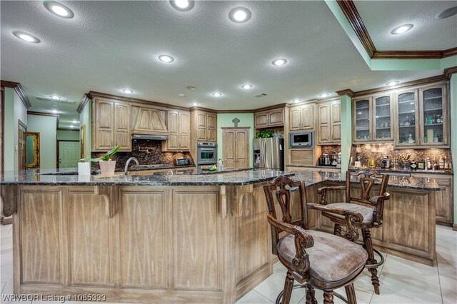 kitchen with a spacious island, dark stone countertops, light tile patterned floors, ornamental molding, and appliances with stainless steel finishes