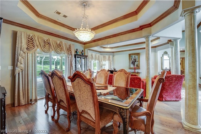 dining space with a raised ceiling, ornate columns, wood-type flooring, and an inviting chandelier