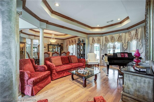 living room featuring decorative columns, a tray ceiling, ornamental molding, and light wood-type flooring