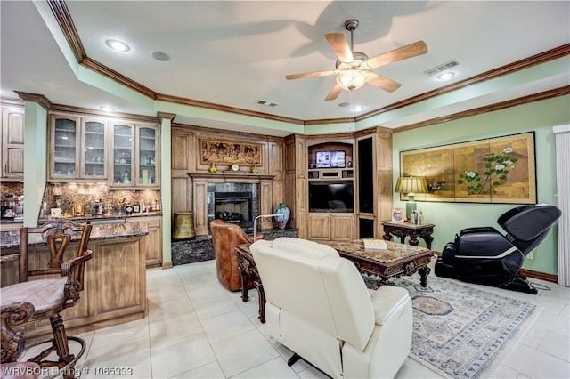 living room with a high end fireplace, a raised ceiling, ceiling fan, crown molding, and light tile patterned flooring