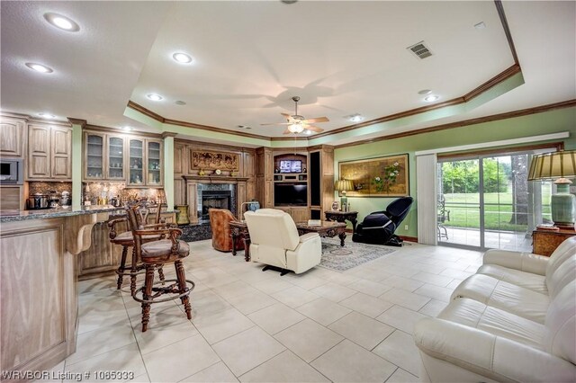 tiled living room with a tray ceiling, ceiling fan, crown molding, and a premium fireplace