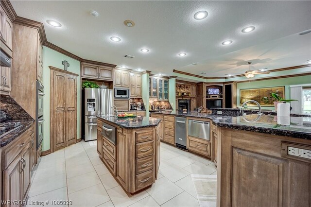 kitchen with backsplash, a kitchen island with sink, dark stone countertops, ornamental molding, and appliances with stainless steel finishes