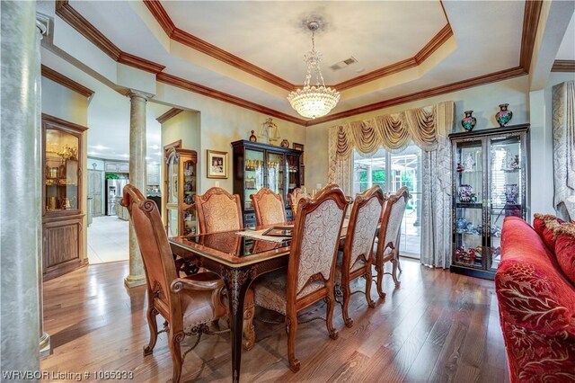 dining space with decorative columns, ornamental molding, a raised ceiling, wood-type flooring, and an inviting chandelier