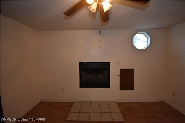 unfurnished living room featuring baseboards, ceiling fan, wood finished floors, and a fireplace