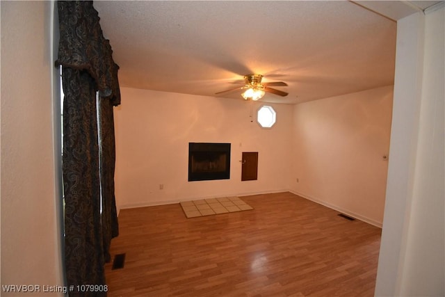 unfurnished living room featuring visible vents, wood finished floors, a fireplace, and a ceiling fan