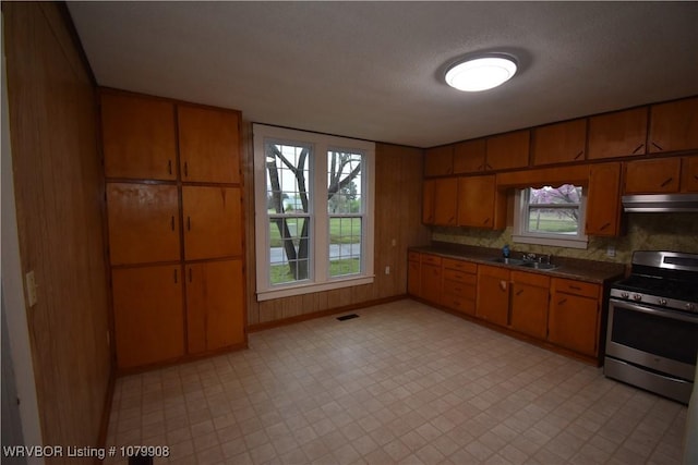 kitchen featuring stainless steel range with electric stovetop, dark countertops, under cabinet range hood, and brown cabinets