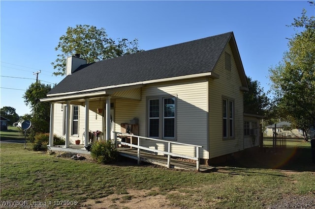 rear view of house featuring covered porch, a shingled roof, a yard, and a chimney