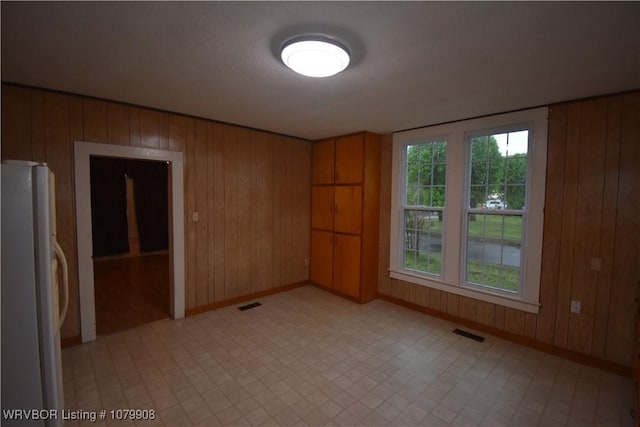 spare room with baseboards, visible vents, light floors, and wood walls