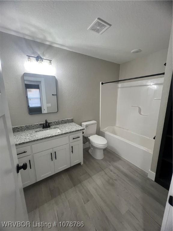 bathroom featuring toilet, vanity, wood finished floors, a textured ceiling, and visible vents