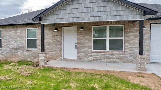 view of exterior entry featuring brick siding and a shingled roof