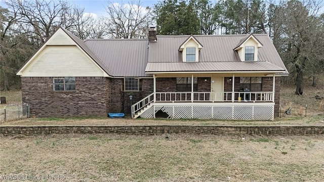 new england style home with a porch, brick siding, metal roof, and a chimney