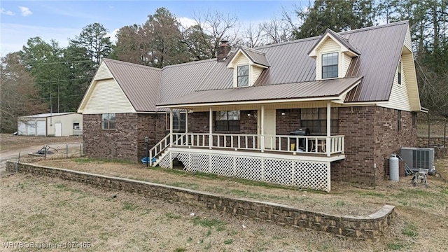 view of front facade with brick siding, a chimney, covered porch, central AC unit, and metal roof