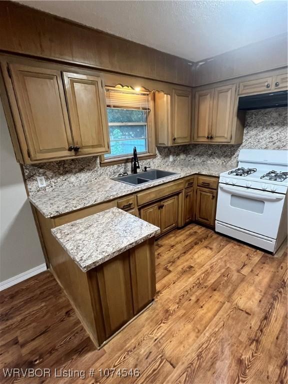 kitchen with wood-type flooring, light stone counters, white gas stove, and sink