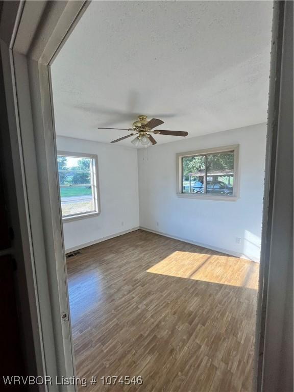 spare room with ceiling fan, plenty of natural light, a textured ceiling, and hardwood / wood-style flooring