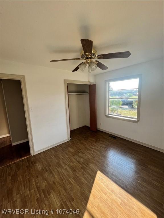 unfurnished bedroom with ceiling fan, dark wood-type flooring, and a closet