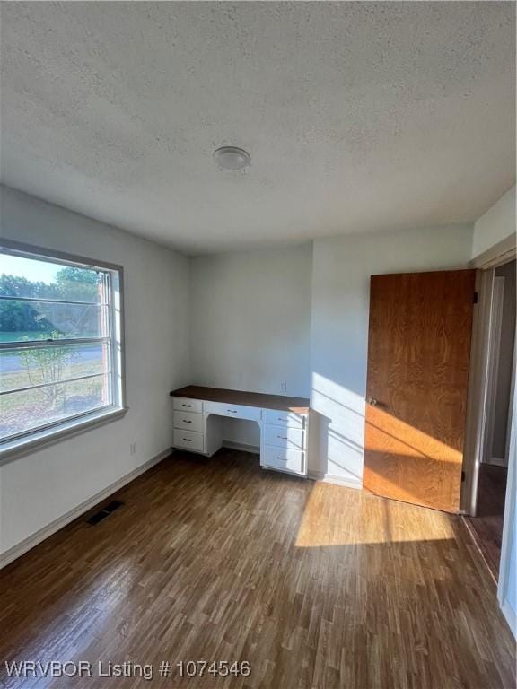 unfurnished office with a textured ceiling, built in desk, and dark hardwood / wood-style floors