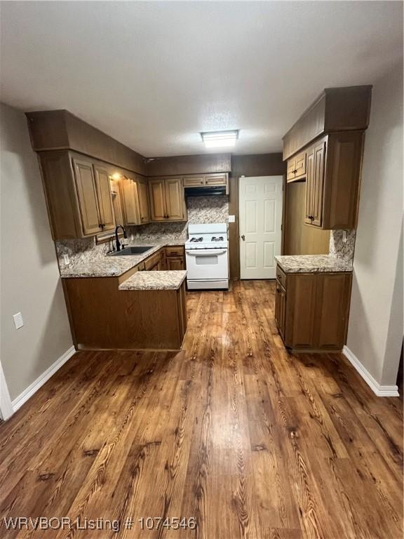 kitchen with sink, dark hardwood / wood-style floors, white range oven, backsplash, and kitchen peninsula