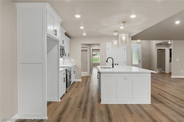 kitchen with appliances with stainless steel finishes, sink, white cabinets, hanging light fixtures, and an island with sink