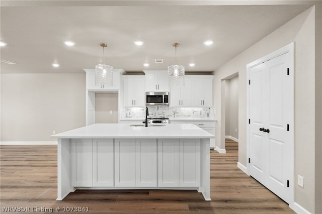 kitchen featuring sink, hanging light fixtures, backsplash, an island with sink, and white cabinets