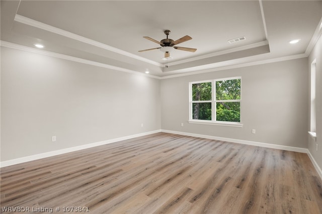 empty room with a tray ceiling, ceiling fan, crown molding, and light hardwood / wood-style floors