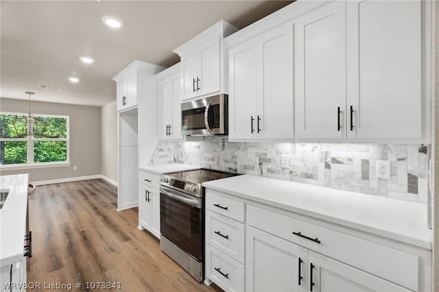 kitchen with backsplash, hanging light fixtures, light hardwood / wood-style floors, white cabinetry, and stainless steel appliances