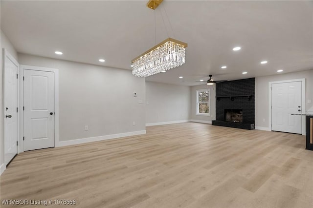 unfurnished living room featuring a brick fireplace, ceiling fan with notable chandelier, and light hardwood / wood-style floors