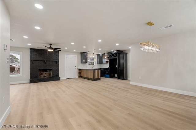 unfurnished living room with a fireplace, ceiling fan with notable chandelier, and light wood-type flooring