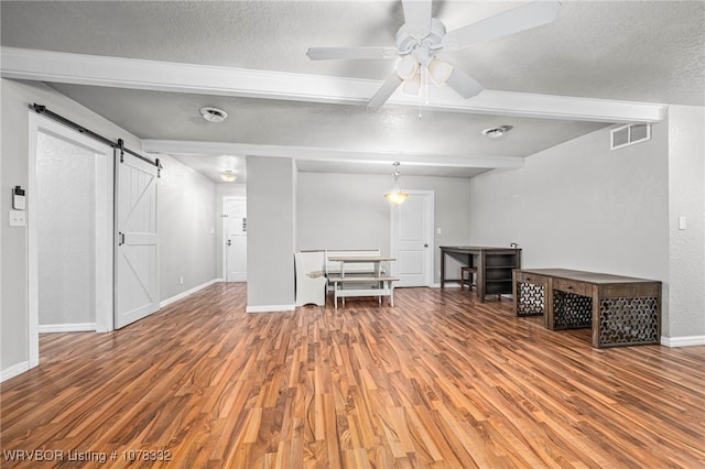 interior space featuring ceiling fan, a barn door, beamed ceiling, a textured ceiling, and hardwood / wood-style flooring