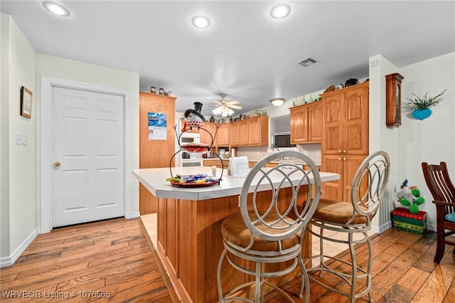 kitchen with a kitchen breakfast bar, a center island with sink, ceiling fan, and light hardwood / wood-style floors