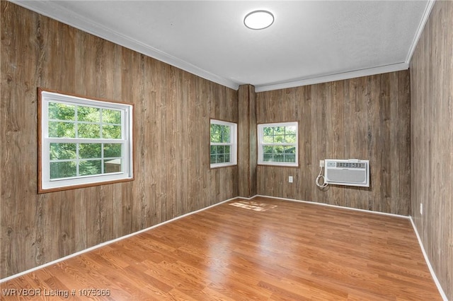 unfurnished room featuring wooden walls, light hardwood / wood-style flooring, an AC wall unit, and ornamental molding