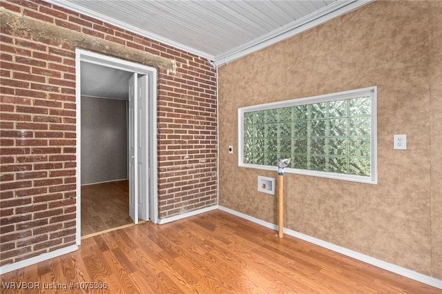 spare room featuring crown molding, light hardwood / wood-style flooring, and brick wall