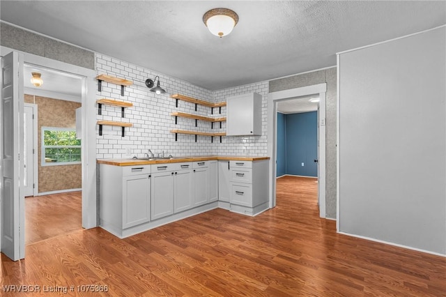 kitchen featuring sink, light hardwood / wood-style flooring, decorative backsplash, butcher block countertops, and white cabinetry