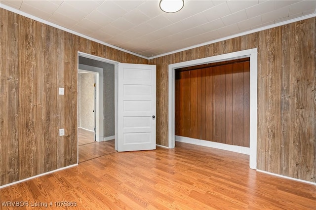 empty room with crown molding, light hardwood / wood-style flooring, and wooden walls