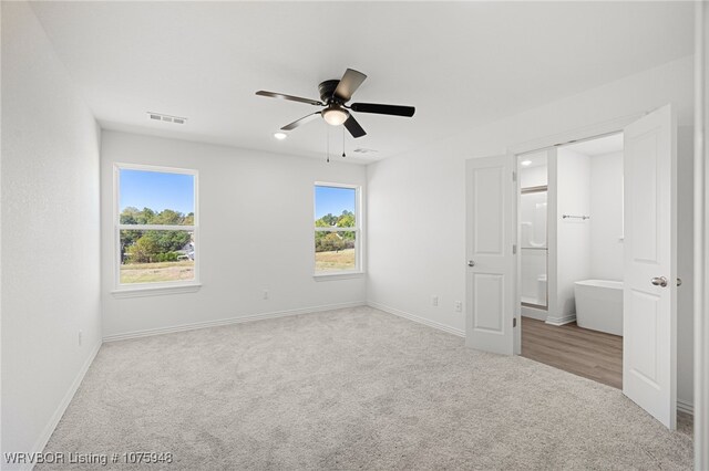 unfurnished bedroom featuring ceiling fan, light colored carpet, and ensuite bath