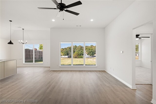 unfurnished living room featuring ceiling fan with notable chandelier and light hardwood / wood-style flooring