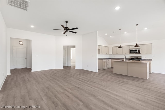 kitchen with light stone countertops, appliances with stainless steel finishes, ceiling fan, pendant lighting, and an island with sink