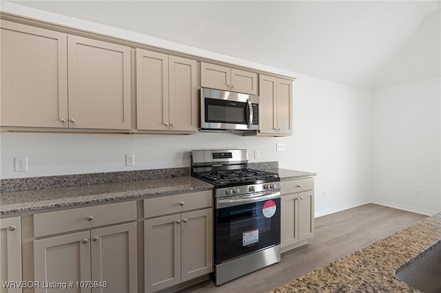 kitchen with hardwood / wood-style flooring, appliances with stainless steel finishes, and dark stone counters