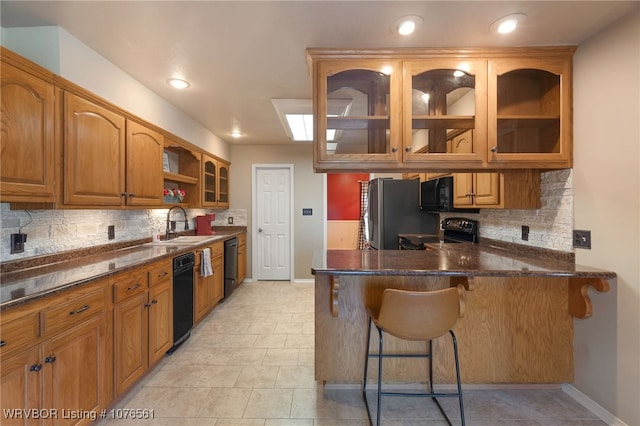 kitchen featuring sink, kitchen peninsula, dark stone countertops, a breakfast bar area, and black appliances