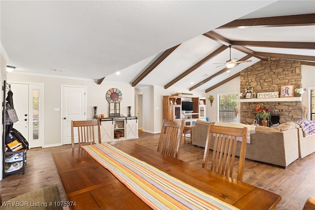 dining area featuring lofted ceiling with beams, hardwood / wood-style flooring, a stone fireplace, and ceiling fan