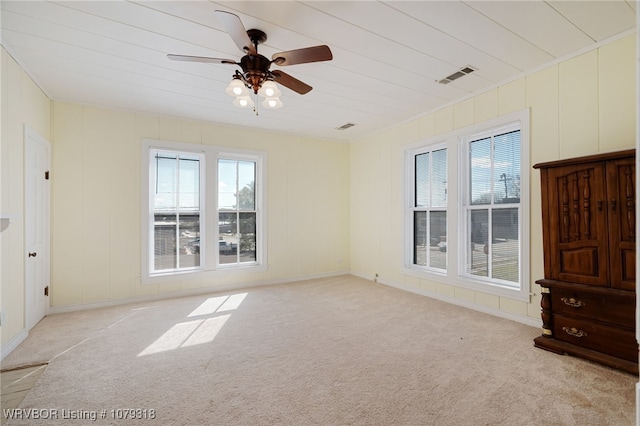 unfurnished room featuring a ceiling fan, visible vents, a decorative wall, and light carpet