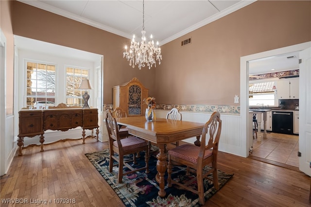 dining room featuring crown molding, wainscoting, visible vents, and light wood-style floors