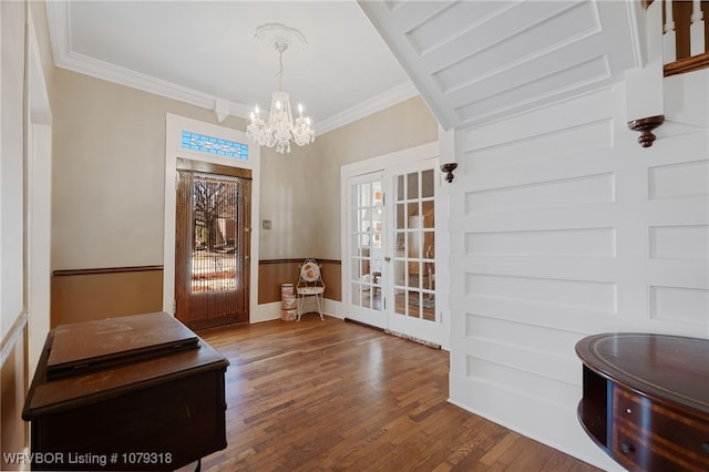 entrance foyer featuring wood finished floors, french doors, ornamental molding, wainscoting, and an inviting chandelier