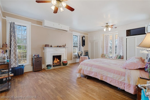 bedroom featuring a fireplace with flush hearth, multiple windows, crown molding, and hardwood / wood-style floors