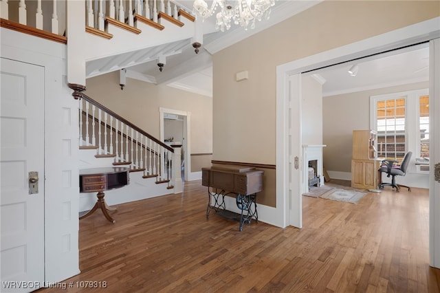 foyer featuring a chandelier, a fireplace, wood finished floors, stairway, and crown molding