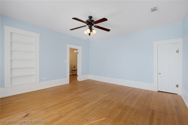 unfurnished room featuring built in shelves, visible vents, light wood-style floors, ceiling fan, and baseboards