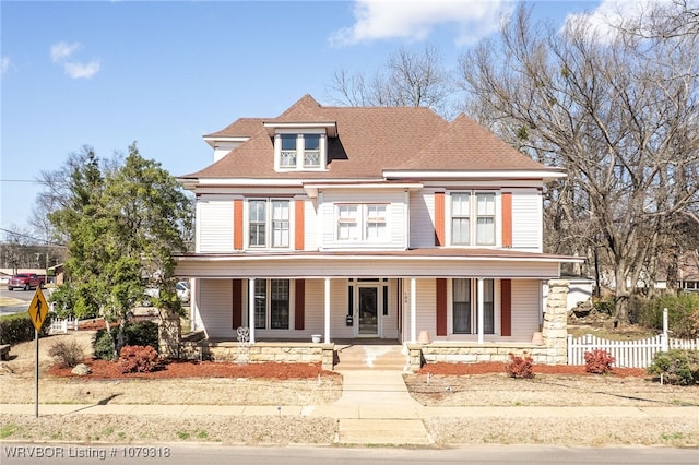 victorian-style house featuring a porch, fence, and a shingled roof