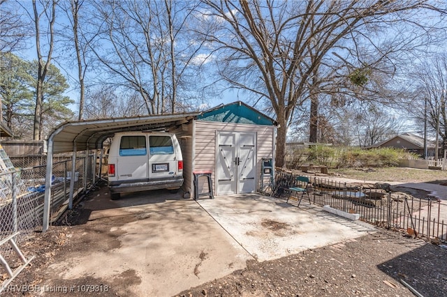 view of outbuilding with concrete driveway, a carport, and fence
